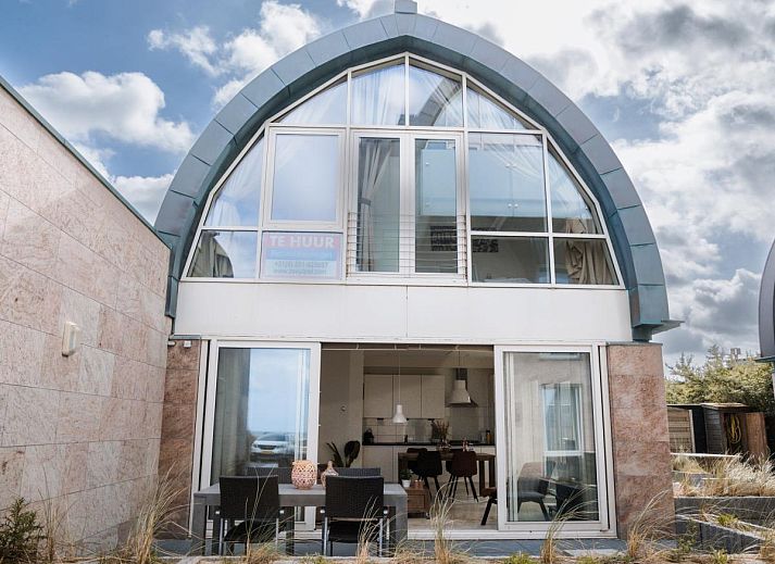Gemuetliches Wohnzimmer des Ferienhauses Zeebaars in Egmond aan Zee an der Nordseekueste mit komfortabler Sitzecke und Blick auf die Terrasse.