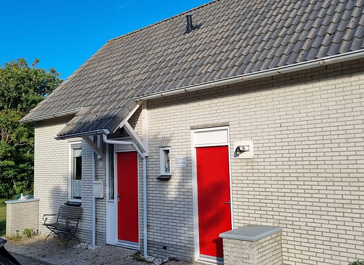 Frontansicht des Ferienhauses NH549 in Callantsoog, Nordseekueste, Nordholland, mit roten Tueren und gruener Umgebung.