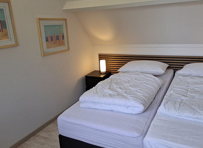 Frontansicht des Ferienhauses NH549 in Callantsoog, Nordseekueste, Nordholland, mit roten Tueren und gruener Umgebung.