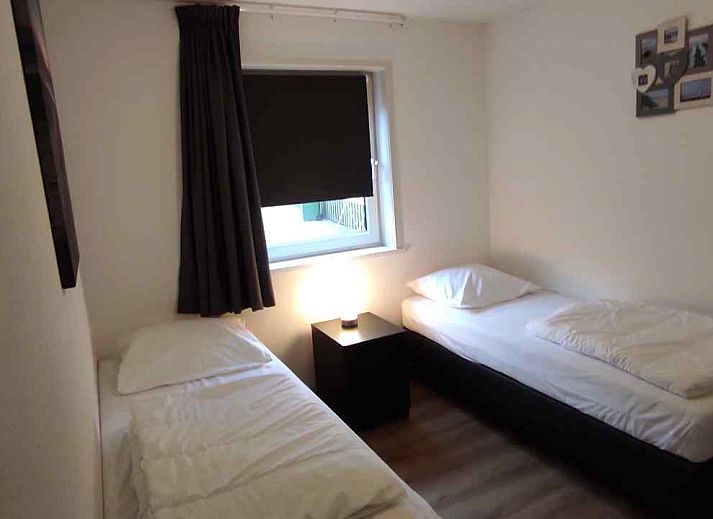 Terrasse des Ferienhauses NH213 in Callantsoog, Nordseekueste, mit Gartenmoebeln aus Holz und gruener Umgebung.