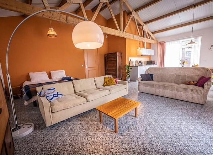 Moderne Kueche im Ferienhaus in Hem, IJsselmeerkueste, Nordholland mit Holztisch und orangefarbener Wand.