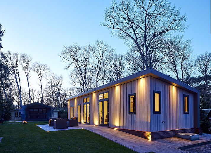 Bungalow te koop in Markelo, Twente, met sfeervol verlicht terras in bosrijke omgeving.