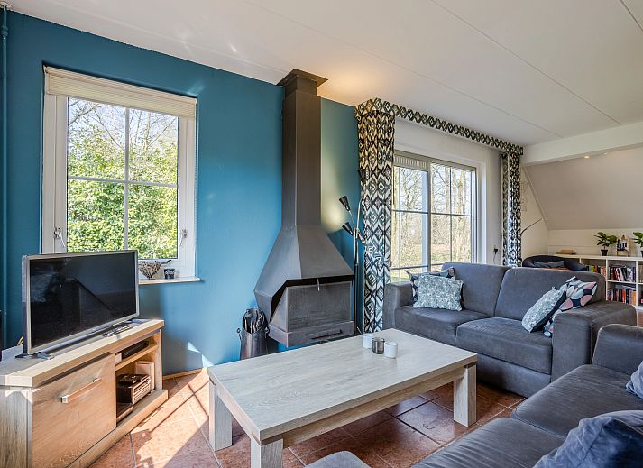 Gezellige woonkamer in Landgoed De Elsgraven bungalow, Enter, Twente, met comfortabele banken en een sfeervolle open haard.