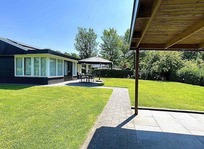 DG630 Ferienhaus in Denekamp, Twente mit sonniger Terrasse und Sonnenschirm auf gruenem Rasen.