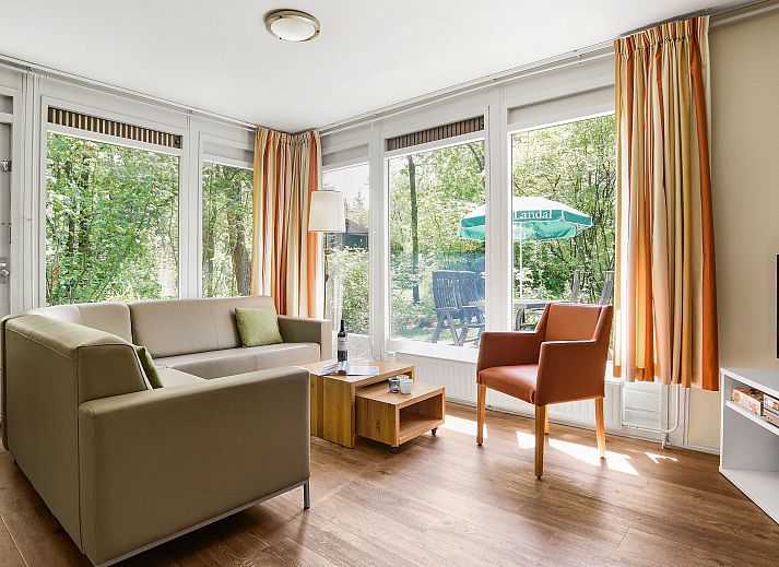 Modernes Wohnzimmer des Bungalows Twenhaarsveld in Holten mit gemuetlicher Sitzecke und Blick auf die Natur.