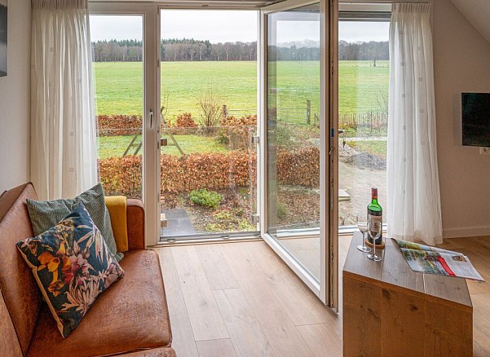 Modern living room in De Buizerd vacation home, Punthorst with large windows and views of the countryside.