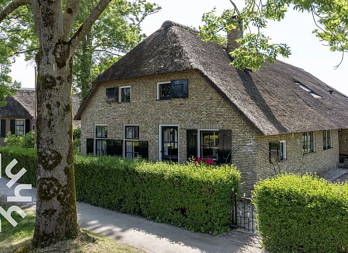 Charmante gevel van OV553 vakantiehuis in Giethoorn, Noordwest Overijssel, met rieten dak en groene heg.