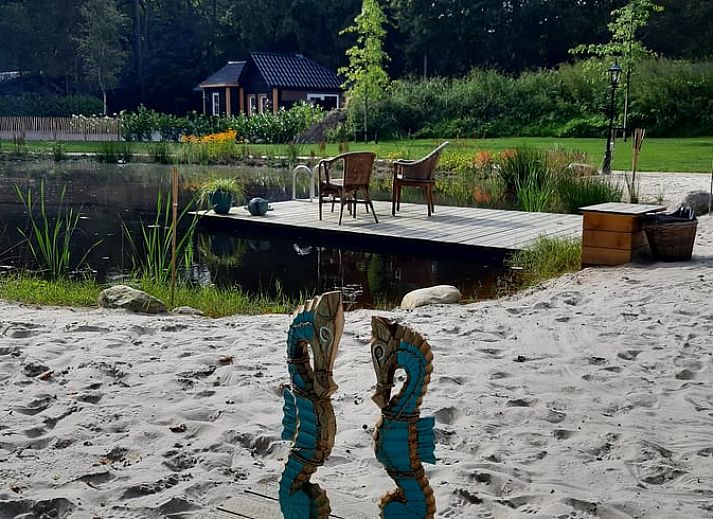 Relax on the sandy beach at Holiday Home in De Bult, Overijssel, overlooking a serene pond and green surroundings.