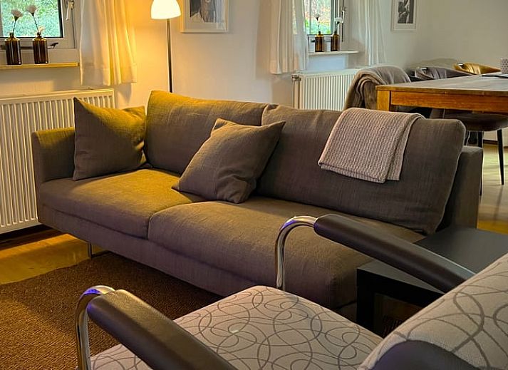 Sonnige Terrasse am Ferienhaus in IJhorst, ausgestattet mit Holztisch und Stuehlen, umgeben von gruener Natur.