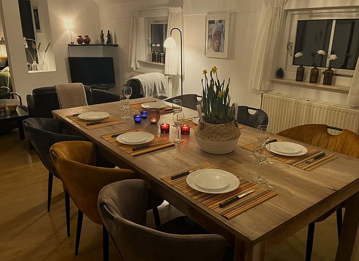 Sonnige Terrasse am Ferienhaus in IJhorst, ausgestattet mit Holztisch und Stuehlen, umgeben von gruener Natur.