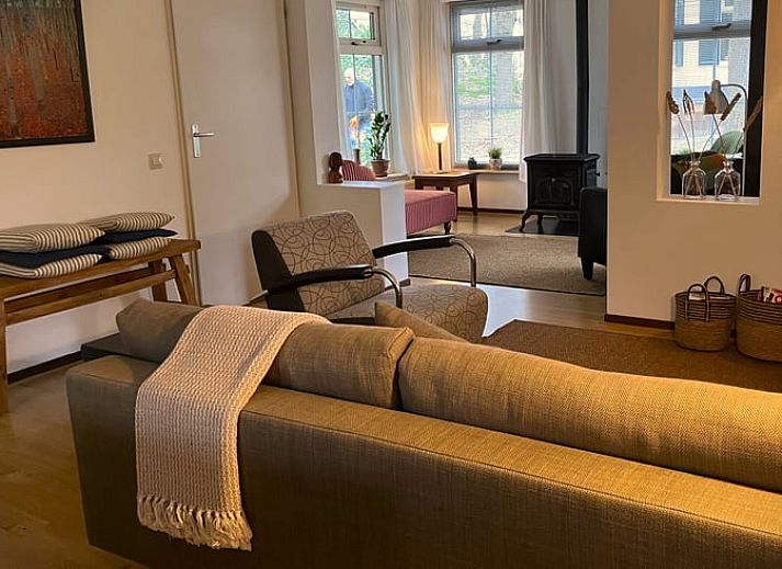 Sonnige Terrasse am Ferienhaus in IJhorst, ausgestattet mit Holztisch und Stuehlen, umgeben von gruener Natur.