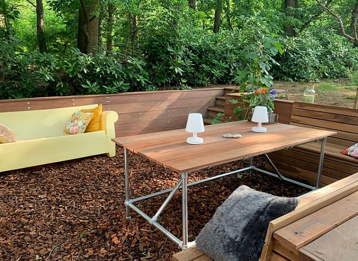 Cozy living room of a cottage in Maarn, Utrechtse Heuvelrug, with a comfortable sofa and a view of the terrace surrounded by nature.