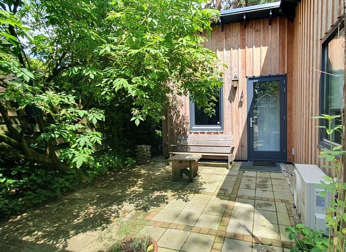 Schaduwrijke patio bij Vakantiehuisje in Bilthoven, Utrecht, met houten bank.