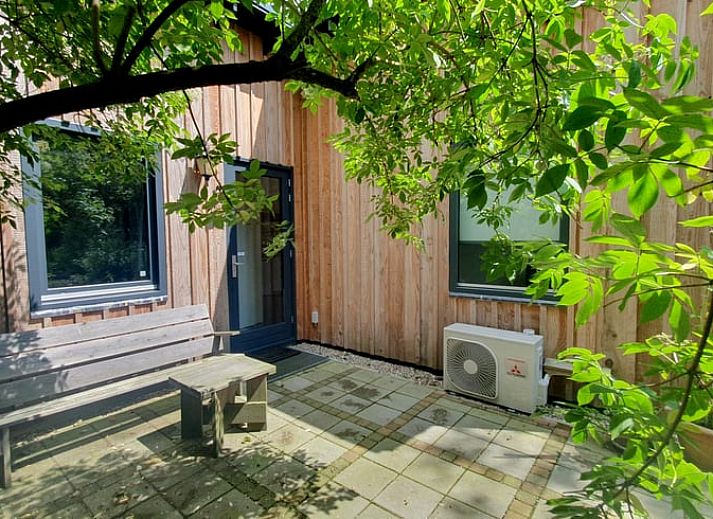 Schaduwrijke patio bij Vakantiehuisje in Bilthoven, Utrecht, met houten bank.