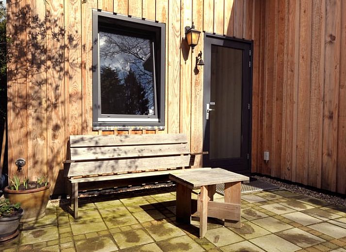 Schaduwrijke patio bij Vakantiehuisje in Bilthoven, Utrecht, met houten bank.