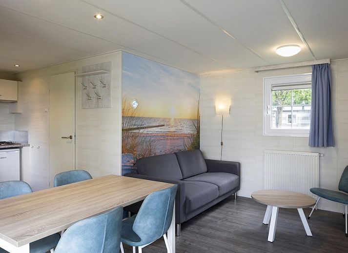 Gezellige woonkamer in chalet RP4B, Kamperland, met moderne keuken en strandthema muurdecoratie.
