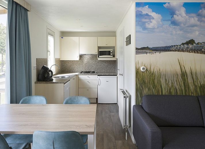 Gezellige woonkamer in chalet RP4B, Kamperland, met moderne keuken en strandthema muurdecoratie.