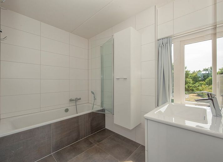 Geraeumiges Wohnzimmer der Villa R10B in Kamperland, Noord-Beveland, Zeeland mit moderner Einrichtung und Blick auf die gruene Umgebung.