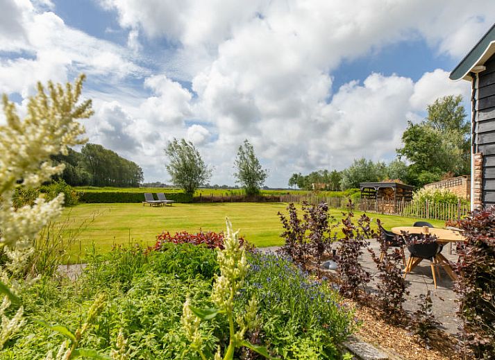 Ruime tuin van Vakantiehuis De kleine Pionier in Grijpskerke, Walcheren, Zeeland met ligstoelen en groene omgeving.