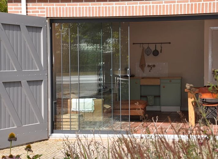 Glazen schuifdeuren openen naar een lichte binnenruimte in Vakantiehuis in Nieuw- en Sint Joosland, Walcheren, Zeeland.