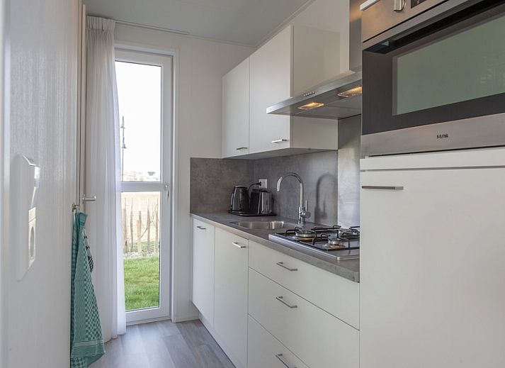 Veranda of L4K Comfort vacation home in Nieuwvliet-Bad, Zeeuws-Vlaanderen, overlooking green surroundings and blue sky.