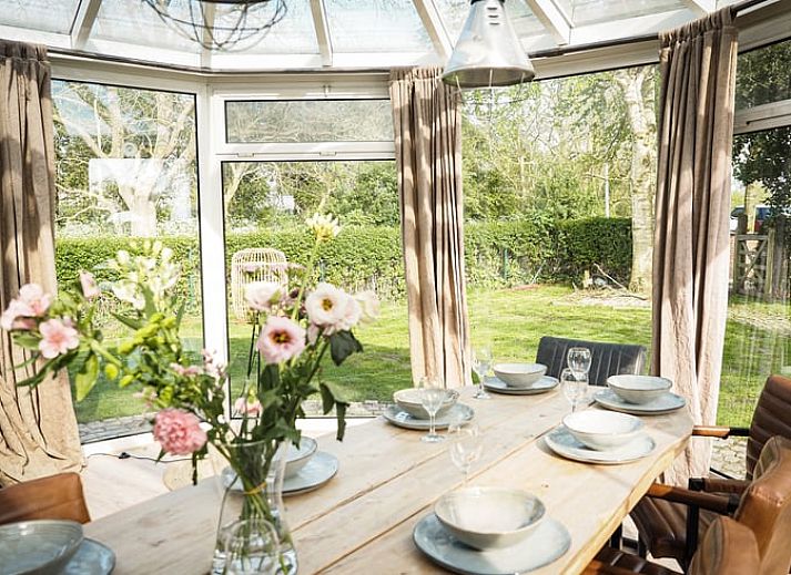 Lichte eetkamer in Vakantiehuis in Sluis, Zeeuws-Vlaanderen, met uitzicht op groene tuin. Perfect voor een ontspannen verblijf in Zeeland.