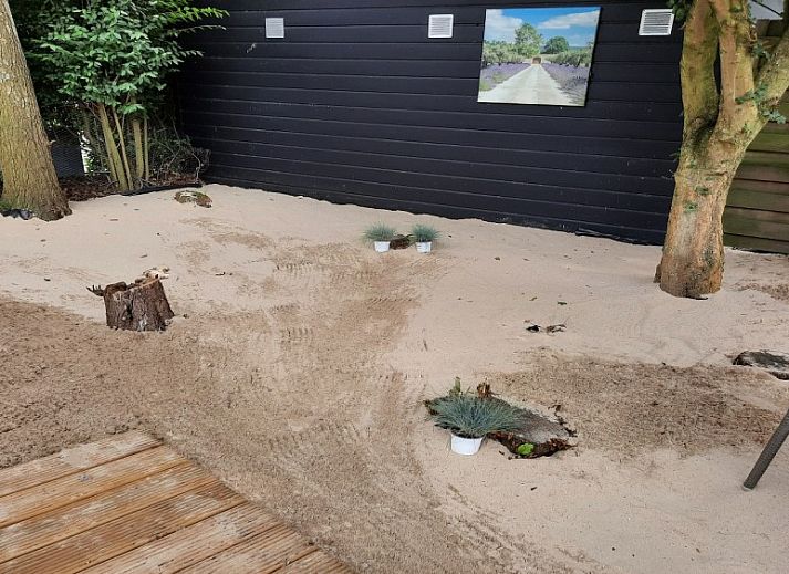 Relax in the quiet sandy garden of Chalet Sunrise in Ouddorp, Zeeland, with comfortable chairs and surrounding nature.