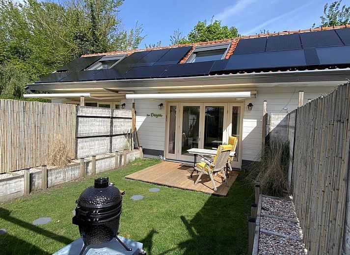 Sonnige Terrasse am Ferienhaus VZ991 in Ouddorp, Suedholland, mit bequemen Stuehlen und gruener Umgebung.