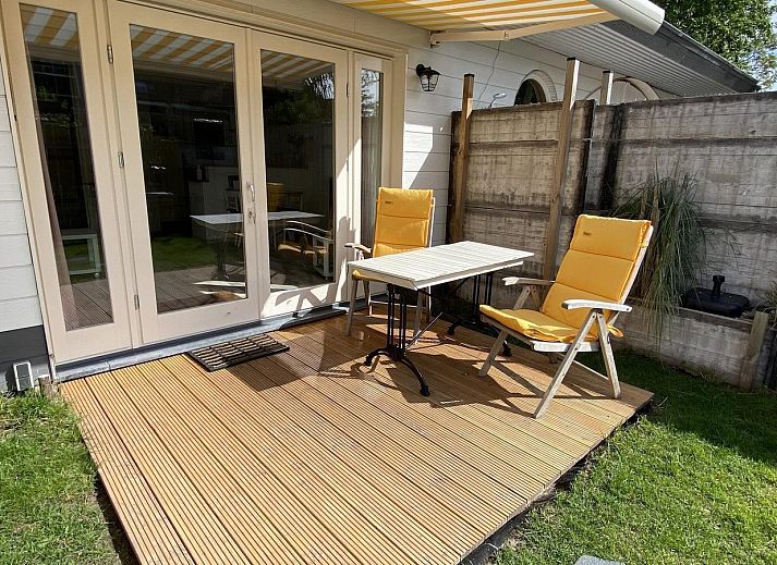 Sonnige Terrasse am Ferienhaus VZ991 in Ouddorp, Suedholland, mit bequemen Stuehlen und gruener Umgebung.