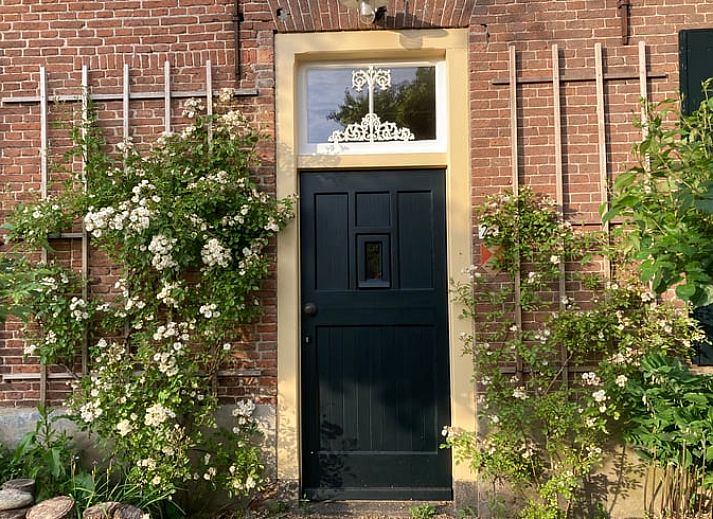 Charmanter Eingang zum Ferienhaus in Balgoij, Rijk van Nijmegen, Gelderland, umgeben von bluehenden Schlingpflanzen und historischen Backsteinen.