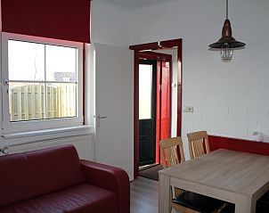 Knusse woonkamer van Onder de vuurtoren 115, Texel, met rode bank en eettafel, ideaal voor een ontspannen verblijf.
