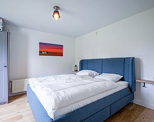 Comfortabele slaapkamer in vakantiehuis Muyweg 062, De Cocksdorp, Texel met groot bed en kunst aan de muur.