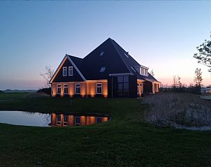 Vakantiehuis Eierland in De Cocksdorp, Texel, straalt in de schemering met sfeervolle verlichting en een vijver.