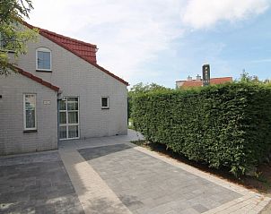 Vooraanzicht van Vakantiehuis D 493 in De Cocksdorp, Texel, met een ruime oprit en groene haag, ideaal voor een ontspannen verblijf op de Waddeneilanden.