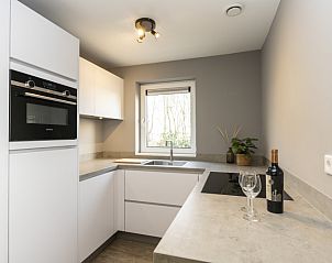 Strakke keuken in Duinoord Texel vakantiehuis, De Cocksdorp, met moderne apparatuur en wijnfles.