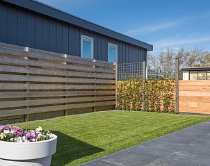 Green garden of Chalet Bregkoog 262, De Koog, Texel, with flowers and wooden fence for privacy.