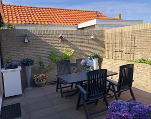 Privterras van Appartement Duinzee Texel in De Koog, met tuinmeubilair en kleurrijke bloemen.