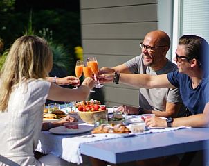 Vriendengroep geniet van maaltijd op terras bij Bungalowpark 't Hoogelandt - Texelboogaloo, De Koog, Texel, in de zon.