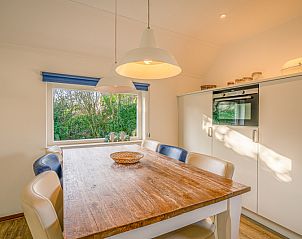 Eetruimte in Vakantiehuis Kamperfoelie 65, De Koog, Texel met houten tafel en tuinzicht.