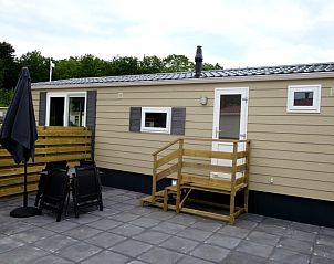 Veranda van Chalet Bregkoog 54 MaMaMia, De Koog, Texel met zitplaatsen en parasol voor ontspannen buitenleven.