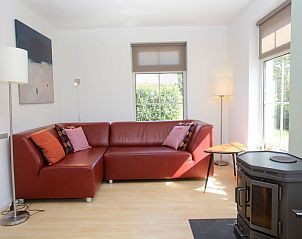 Gezellige woonkamer in T8A bungalow, De Koog, Texel met comfortabele rode bank en veel natuurlijk licht, perfect voor ontspanning.