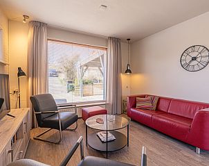 Gezellige woonkamer in De Zandduyn, De Koog, Texel, met comfortabele rode bank en grote ramen met uitzicht op de tuin.