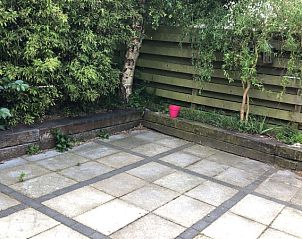 Ruim buitenterras van Kamerstraat 39, vakantiehuis De Koog, Texel omringd door groen en houten schutting.