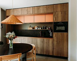 Moderne keuken en eetruimte in Luxe Appartement 4p, Den Burg, Texel met houten afwerking en rotanlamp.