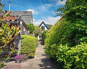 Groene tuinpad naar Appartement De Merel in Den Burg, Texel, omgeven door weelderige planten en bloemen.