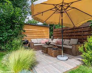 Knusse zithoek in de tuin van Huisje in Den Burg, Texel, met schaduwrijke parasol.