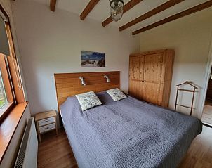 Knusse slaapkamer in Vakantiehuis Duinzicht, Den Burg, Texel, met houten meubels en een serene sfeer.