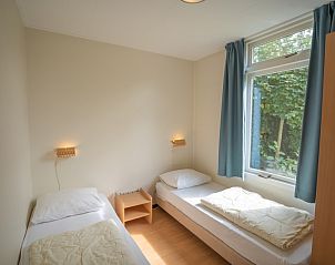 Sfeervolle slaapkamer met twee bedden in Bungalow Uterste Coogh 98, De Dennen, Texel met uitzicht op de tuin.