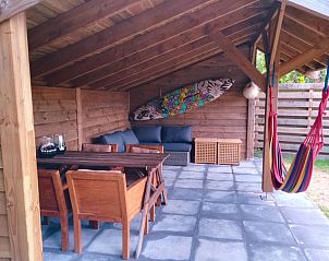 Overdekte zithoek bij Vakantiepark De Koorn-aar - Chalet 102 type C, De Dennen, Texel met comfortabele meubels en kleurrijke hangmat.