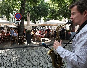 Levendige straatmuzikant bij Derlon Hotel Maastricht, vakantieappartement in Maastricht, Zuid Limburg, met terrasbezoekers.